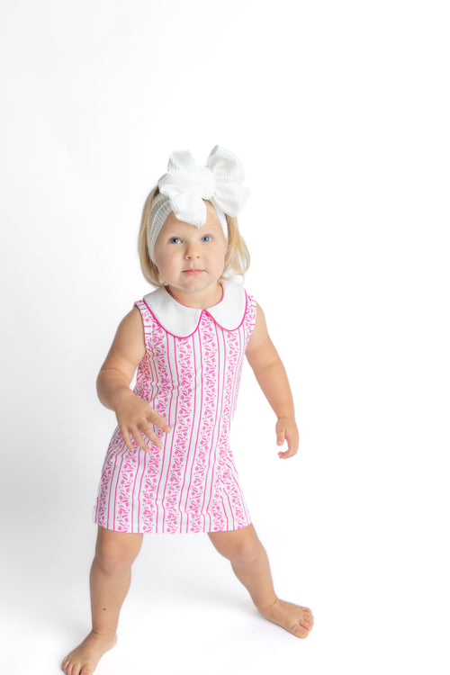 Young girl wearing a pink dress with white collar and a white headband on a white background