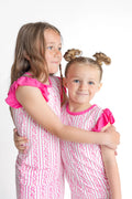 Two young girls in matching pink and white outfits hugging on a white background