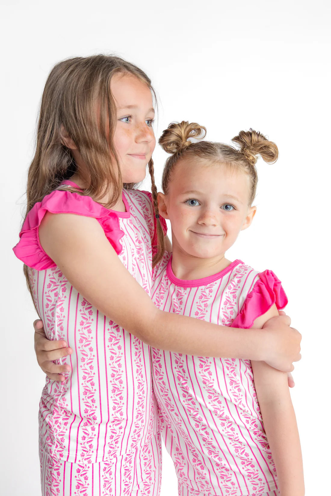 Two young girls in matching pink and white outfits hugging on a white background