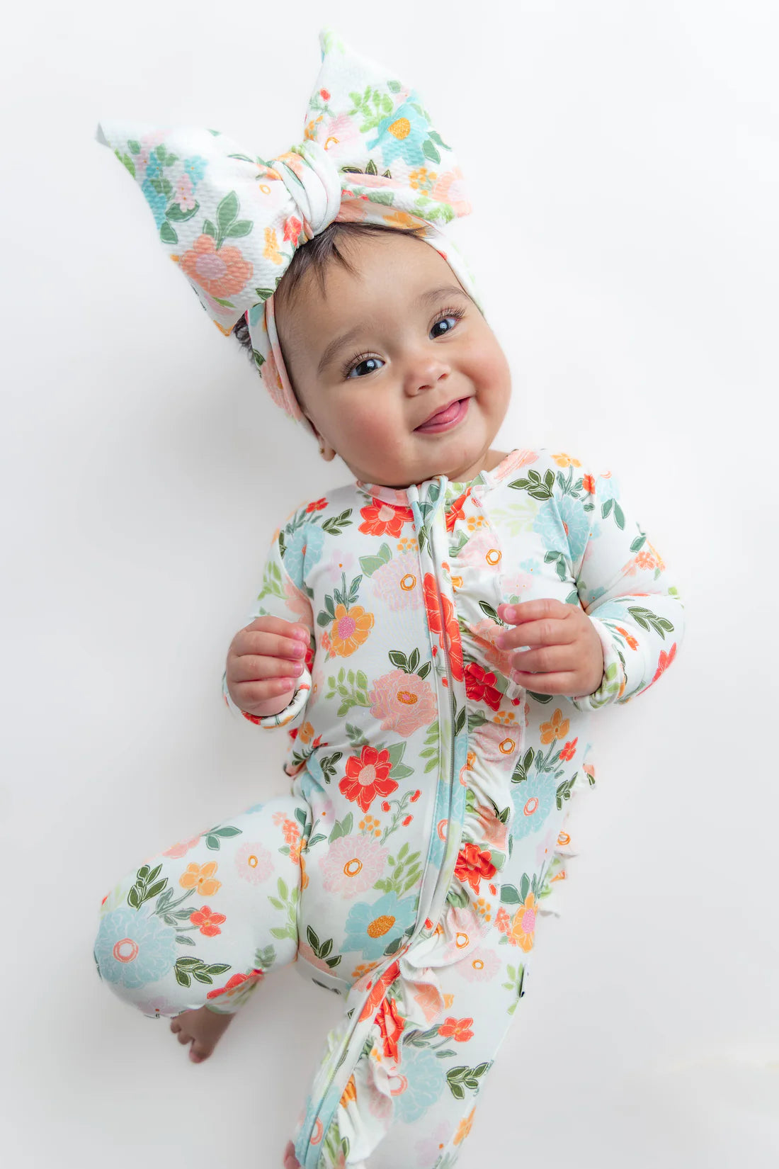 Baby wearing a floral onesie and headband on a white background