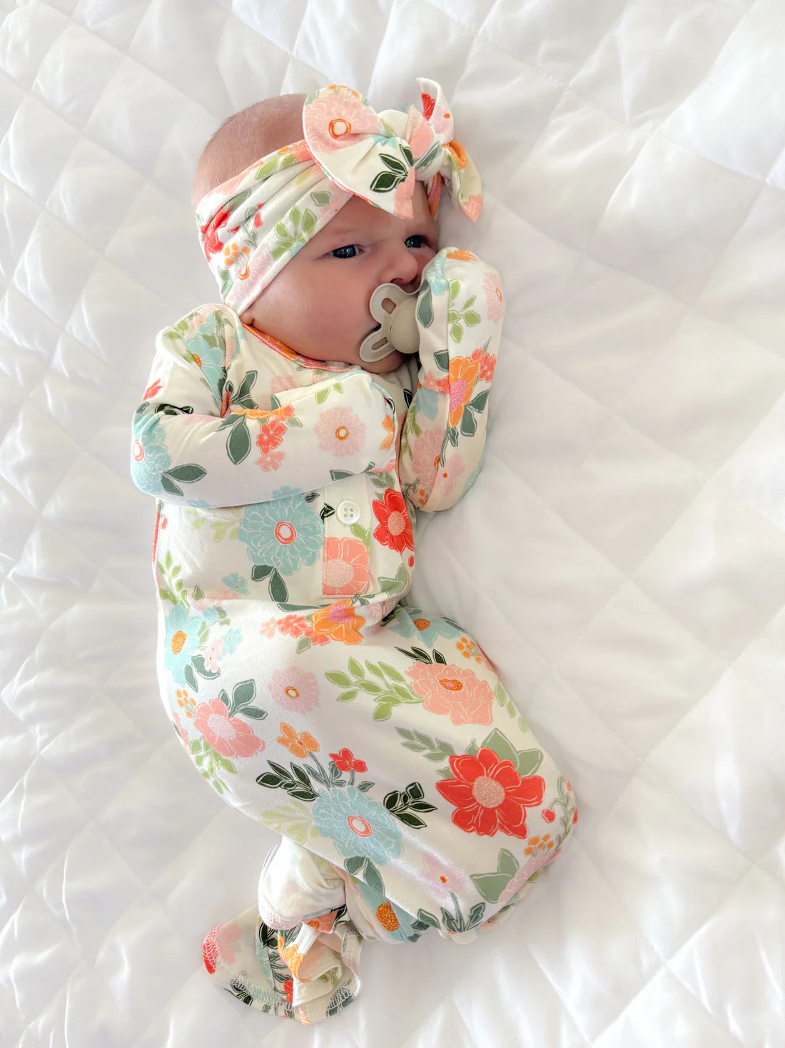 Baby swaddled in a floral blanket with a matching headband on a white background