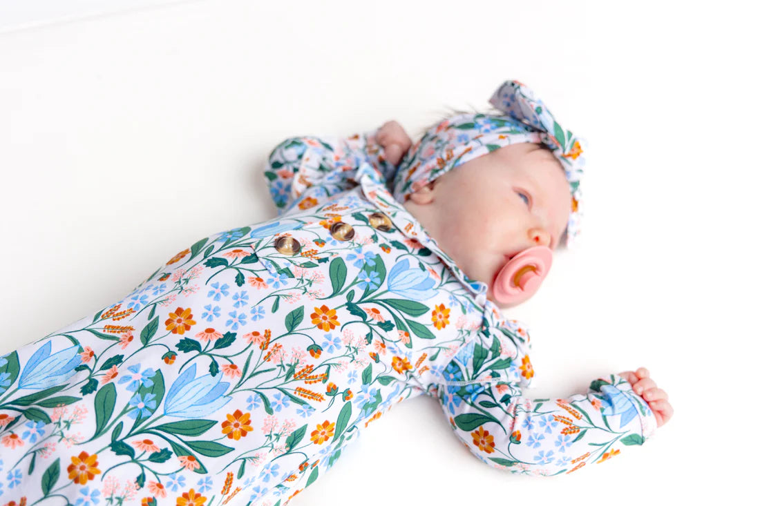 Baby sleeping in a floral knotted gown on a white background
