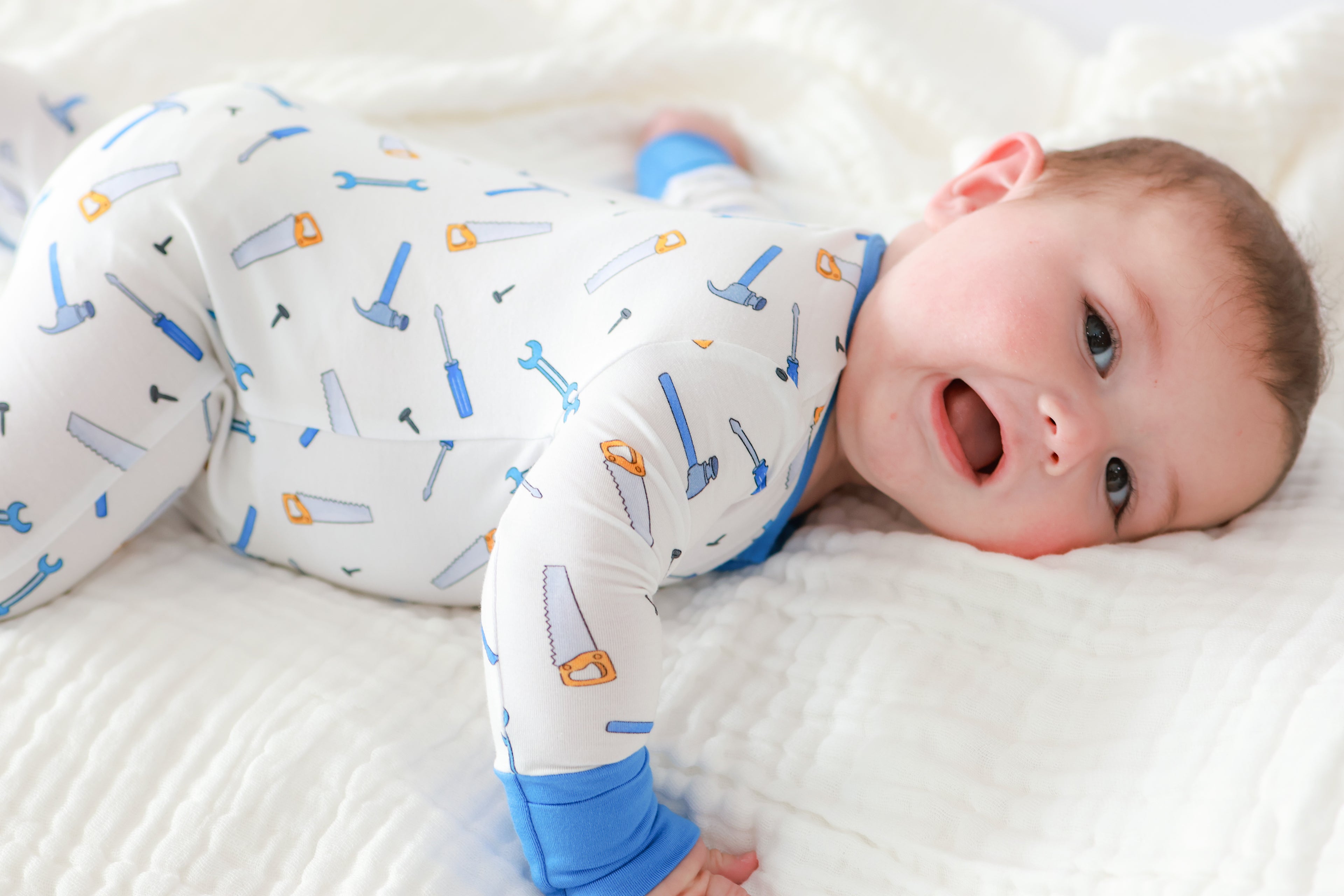 Baby wearing a onesie with tool pattern lying on a white surface
