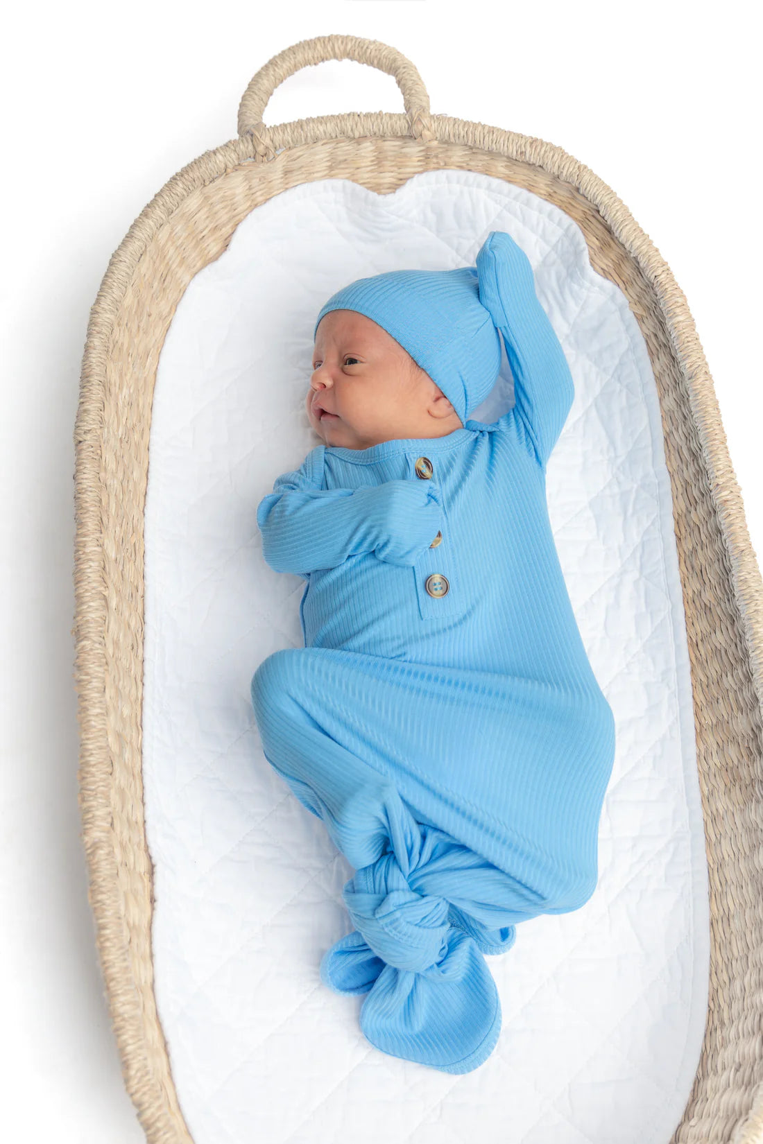 Newborn baby wrapped in blue swaddle and bonnet lying in a wicker basket.