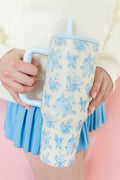 Person holding a floral-patterned tumbler with a straw on a pink background