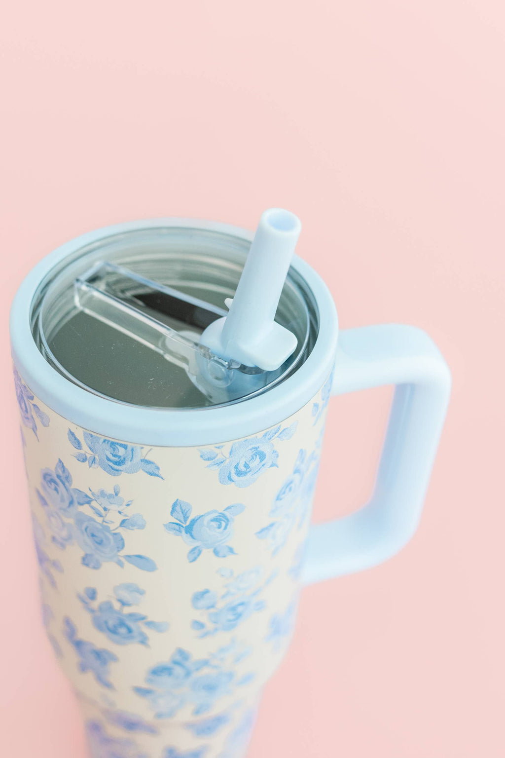 Tumbler with floral pattern, blue handle, and straw on a pink background